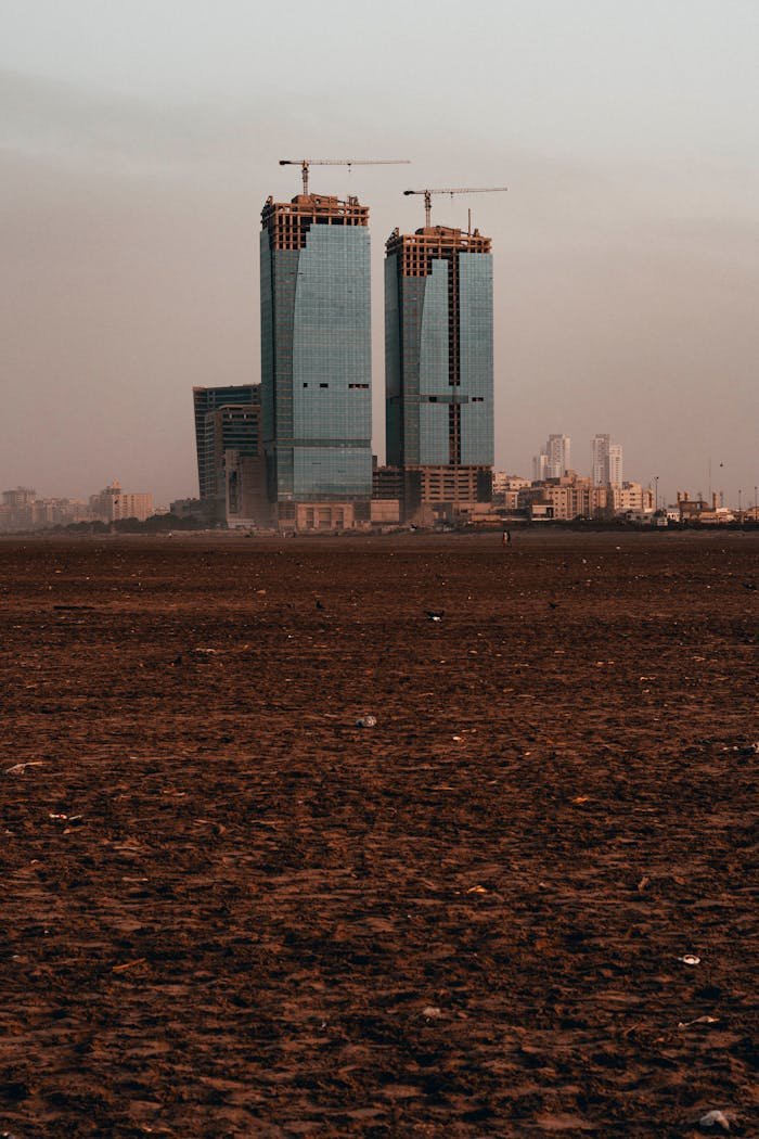 Skyscrapers under construction in a cityscape during daytime with construction cranes on top.